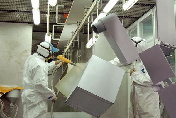Metal furniture components suspended in an industrial coating booth during surface finishing.